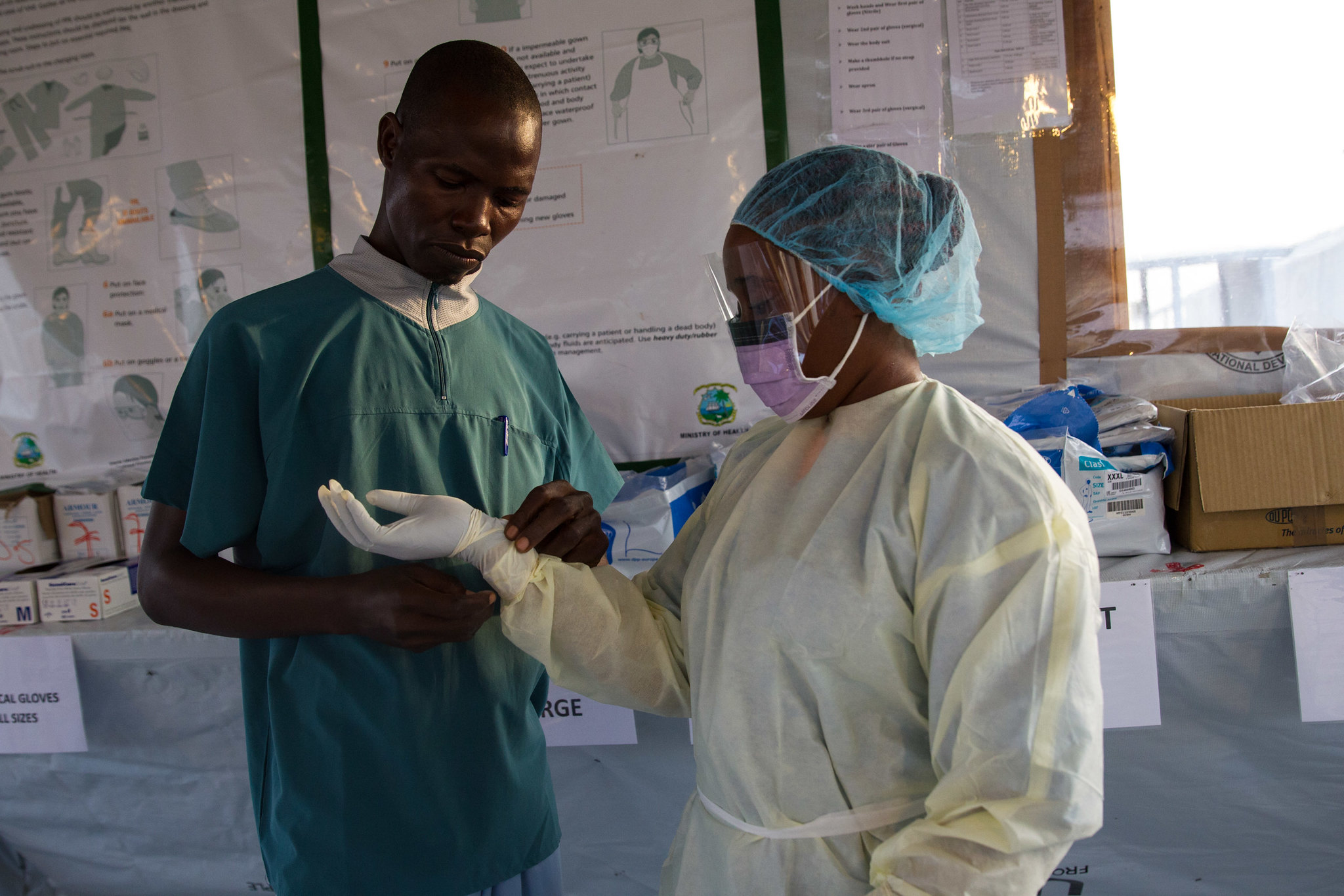 Siah Tamba puts on a light personal protective equipment (PPE). She is an Ebola survivor who now works at the Ebola treatment unit (ETU) in Sinje, Grand Cape Mount, Liberia, after losing her mother, sister, and daughter. The facility is operated by the International Organization for Migration (IOM) in partnership with Liberia's Ministry of Health and Social Welfare (MOHSW) and supported by USAID's Office of U.S Foreign Disaster Assistance. It opened with a capacity of 10 beds, but can rapidly scale to provide care to up to 50 people. The ETU is staffed with 23 medical professionals from Kenya, South Africa, Tanzania, Uganda and Ukraine, as well as 114 Liberians from Grand Cape Mount county, who were recruited and trained to offer clinical and non-clinical care within the facility. The staff received training from the World Health Organisation (WHO) and the MOHSW, and experienced hands-on training at the IOM-managed ETU in Tubmanburg, Bomi County, Liberia.